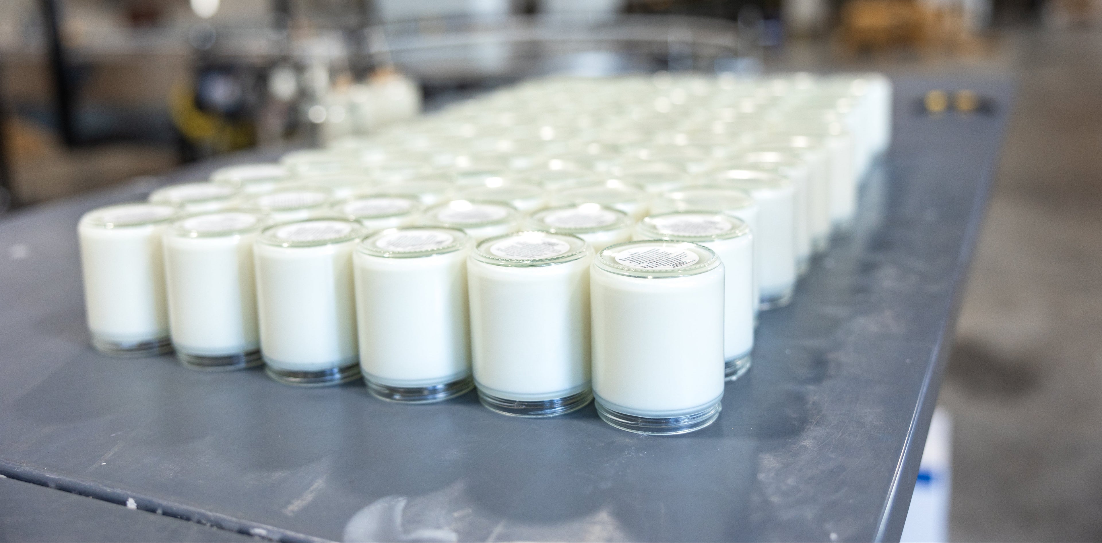 Rows of small containers filled with candle wax on a production line.